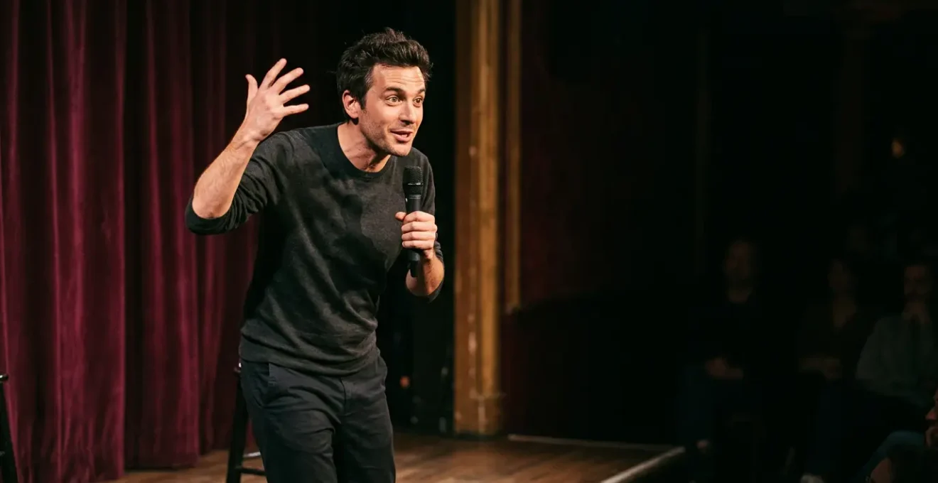 Artiste comique sur scène captivant le public avec un geste théâtral dans une atmosphère intimiste