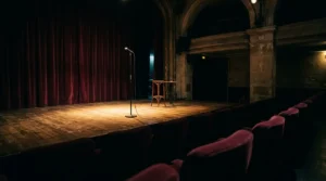 Scène de stand-up parisienne dans la pénombre avec microphone au premier plan et éclairage théâtral