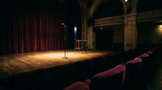 Scène de stand-up parisienne dans la pénombre avec microphone au premier plan et éclairage théâtral